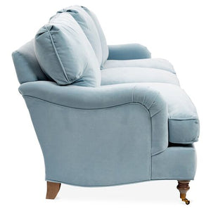 A side view of the Brooke 6-Seat Sofa showcases its plush, light blue fabric with two large back cushions and elegant wooden legs. The sofa exudes a soft, comfortable appearance, featuring a design with gracefully curved armrests.