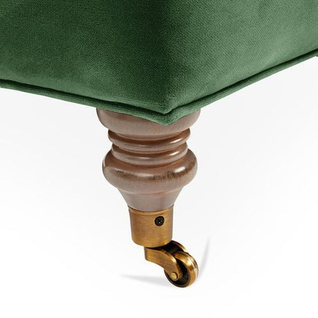 Close-up of the Brooke 6-Seat Sofa's green upholstery, showcasing a corner with a polished wooden leg that is slightly curved and features a brass-colored caster wheel for easy movement.
