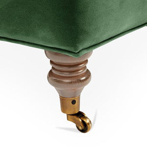 Close-up of the Brooke 6-Seat Sofa's green upholstery, showcasing a corner with a polished wooden leg that is slightly curved and features a brass-colored caster wheel for easy movement.