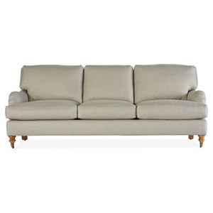The Brooke 6-Seat Sofa is a beige piece with a classic design, featuring three cushions, rolled arms, and wooden legs on casters. Its fabric appears soft and comfortable, making it ideal for a living room setting.