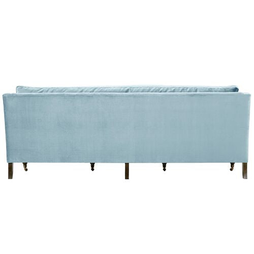 The Margot Velvet Sofa, in a light blue hue, showcases a rectangular design when viewed from the back. It features a high backrest and wooden legs that contribute to its modern and elegant look.