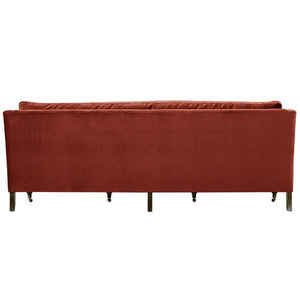 The image features the back view of the Margot Velvet Sofa in red, showcasing its wooden legs. The sofa boasts a simple and modern design.