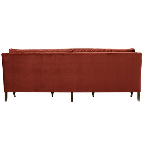 The image features the back view of the Margot Velvet Sofa in red, showcasing its wooden legs. The sofa boasts a simple and modern design.