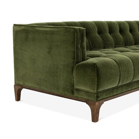 Displayed is the Caledonia Sofa in Sapphire Olive Velvet, featuring a modern design with tufted upholstery. It boasts a low back and seat paired with wooden legs, visible from a side angle.