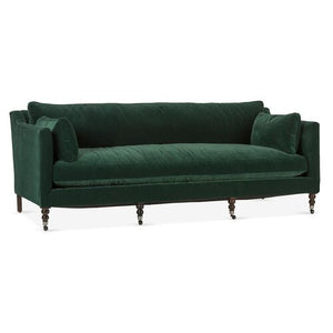 Introducing the Margot Velvet Sofa, a plush and elegant piece in deep green velvet. This classic design features wooden legs and includes two matching cylindrical pillows at each end. It boasts a high back and low armrests for a timeless aesthetic.