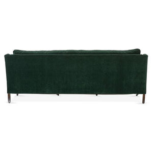 A Margot Velvet Sofa in dark green velvet is showcased from the back, highlighting its sleek, rectangular design and wooden legs. The image captures the sofa in a well-lit environment against a simple background.