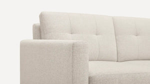 The Nomad Fabric Sofa features a beige color with a tufted backrest and sleek, minimalist design. It includes slightly curved armrests, and its upholstery boasts a finely woven texture for a modern and comfortable look.