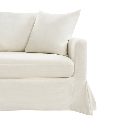 A close-up view of the Torsten Modern Comfortable Sofa in a cream color, featuring a skirted base and a matching cushion. The soft and plush fabric gives it a cozy and inviting appearance. The armrest is slightly rounded, set against a white background.