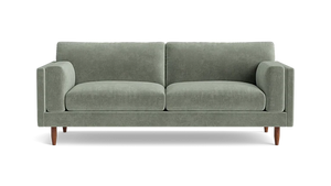 The Skinny Fat 85" Sofa Standard Depth is a stylish, modern sofa in green, featuring two matching cylindrical cushions and wooden legs, set against a plain black background.