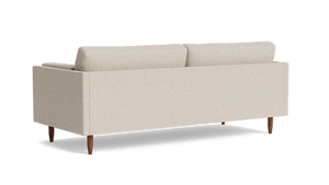 The Skinny Fat 85" Sofa Standard Depth is displayed from the back, showcasing its minimalist design with two plush cushions and wooden legs, all set against a plain black background.