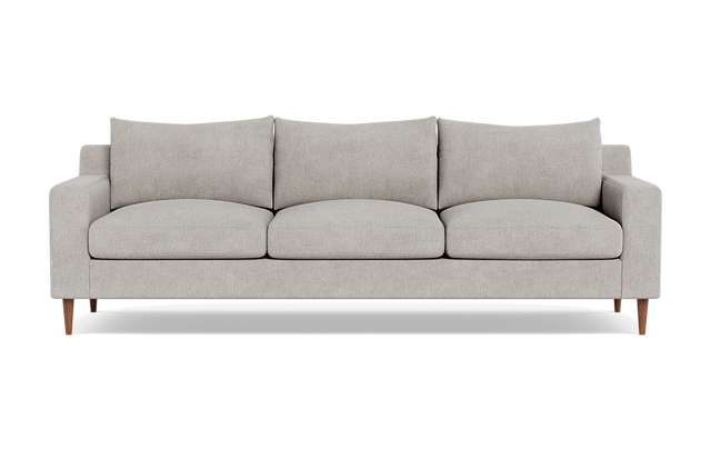The Sloan Custom 3-Seat 95" Sofa features a modern design with a light gray finish, encompassing three seat cushions and three back cushions. Its clean, simple lines and wooden legs contribute to its minimalist and stylish look. The sofa is presented against a plain black background.
