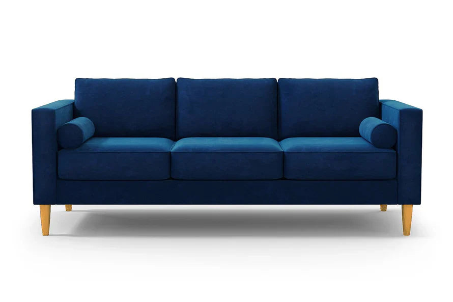 The Samson Sofa is a modern piece with a dark blue fabric, wooden legs, and three cushions. It features two cylindrical pillows positioned at each end, all set against a plain white background.