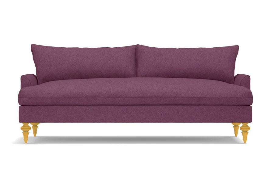 The Saxon Sofa is a sleek design in a plum color, featuring two back cushions and wooden legs. Its smooth, modern upholstery adds a touch of elegance to any room.