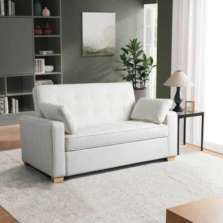 A modern living room featuring the Serta Monroe Full Size Convertible Sofa in white with cushions, a black side table topped with a beige lamp, a small plant, and built-in shelves filled with books and decor. The walls are green, and a large rug covers the wooden floor.