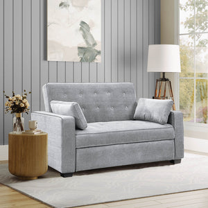 A cozy living room features a Serta Monroe Full Size Convertible Sofa in light gray with button tufting and matching cushions. A wooden side table holds a vase of flowers, accompanied by a modern floor lamp near a large window showcasing a view of greenery. Wall art decorates the gray-paneled wall.