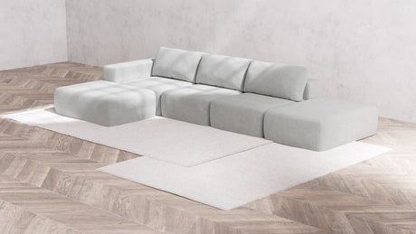 An elegant Modular 3-Seater Open-End Chaise Sectional in Boucle Aspen is arranged on a neutral-toned area rug. The sectional features several square and rectangular pieces, set in a minimalist room with wood-patterned flooring and plain walls.