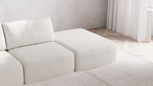 A minimalist living room showcases the Modular 3-Seater Open-End Chaise Sectional in Boucle Aspen, elegantly placed on a white rug. The space is enhanced by light wood flooring and sheer white curtains, contributing to a bright and serene atmosphere.