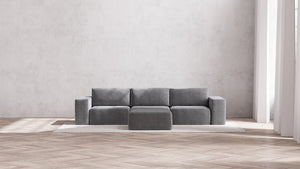 A minimalist living room with a Modular 3-Seater Sofa and Ottoman in Aspen Boucle is set on a light area rug. The space features large windows that flood the hardwood floor with natural light, complemented by plain white walls for an airy and modern feel.