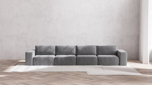 A modern, minimalist living room showcases the Modular 4-Seater Sofa in Boucle Aspen, positioned against a light gray wall. The sofa rests atop a large, light-colored area rug laid over a wooden herringbone floor, cultivating a serene and airy ambiance.