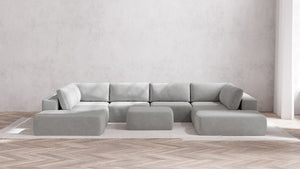 A spacious living room showcases a modern Modular 8-Seater Open-Ends U Sectional + Ottoman in Boucle Aspen, arranged on a white rug. The room embraces a minimalist design with pale, textured walls and wooden herringbone flooring.