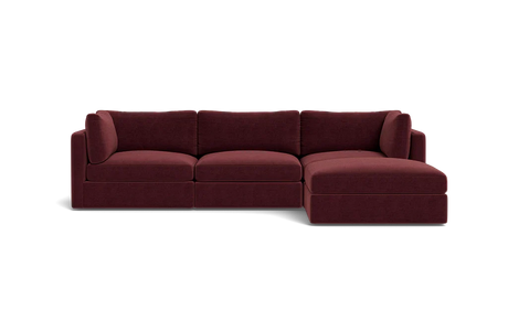 The Tatum Modular 3 Seat Chaise 106" Sectional, with its maroon upholstery and plush cushions, is showcased against a solid black backdrop. This stylish design includes three connected seats and a chaise lounge positioned on the right side.
