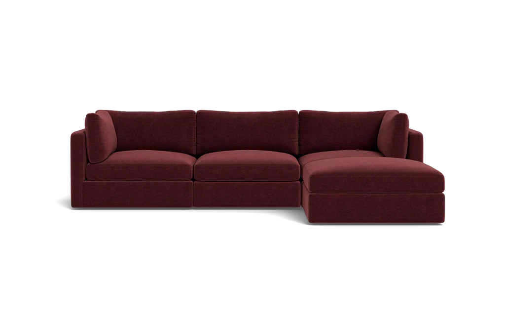 The Tatum Modular 3 Seat Chaise 106" Sectional, with its maroon upholstery and plush cushions, is showcased against a solid black backdrop. This stylish design includes three connected seats and a chaise lounge positioned on the right side.