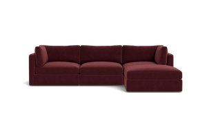 The Tatum Modular 3 Seat Chaise 106" Sectional, with its maroon upholstery and plush cushions, is showcased against a solid black backdrop. This stylish design includes three connected seats and a chaise lounge positioned on the right side.