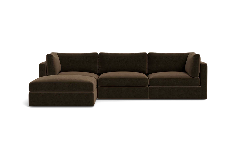 The Tatum Modular 3 Seat Chaise Sectional, featuring a large, dark brown design with cushioned seats and backrests, is displayed against a solid black background. It includes a chaise lounge on the left side, offering ample seating space.