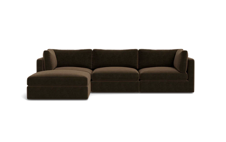 The Tatum Modular 3 Seat Chaise Sectional, featuring a large, dark brown design with cushioned seats and backrests, is displayed against a solid black background. It includes a chaise lounge on the left side, offering ample seating space.