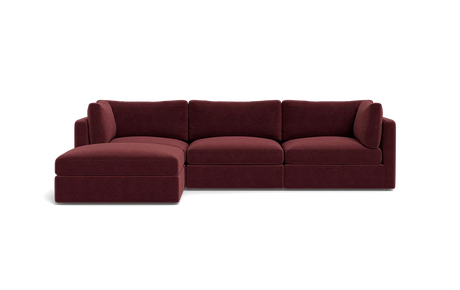 The Tatum Modular 3 Seat Chaise Sectional, upholstered in maroon, sits against a solid black background. It boasts plush cushions and a chaise lounge on the left side, providing a modern and comfortable seating option.