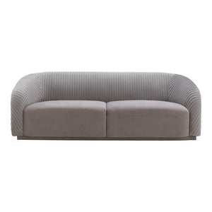 The Yara Pleated Velvet Sofa by Inspire Me! Home Decor features a gray upholstery with a ribbed texture on the back and sides. Its modern, rounded design and smooth cushions provide a clean and contemporary appearance.