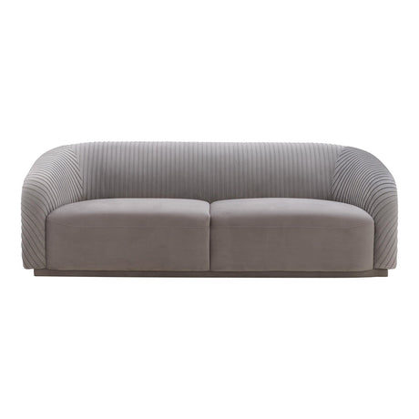 The Yara Pleated Velvet Sofa by Inspire Me! Home Decor features a gray upholstery with a ribbed texture on the back and sides. Its modern, rounded design and smooth cushions provide a clean and contemporary appearance.