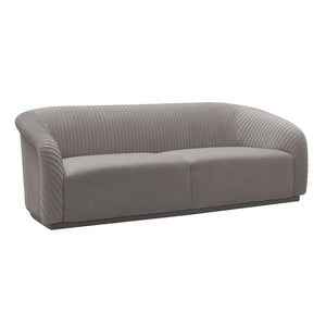 The Yara Pleated Velvet Sofa by Inspire Me! Home Decor is a contemporary piece featuring a rounded backrest and armrests. It is upholstered in modern gray velvet with a vertically stitched pattern, making it a sleek addition that complements various interior styles.