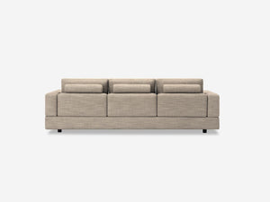 A beige Stage Track Sofa with a minimalist design, featuring three seat cushions and three back cushions, set against a plain white background. Its low profile is complemented by simple, block-like armrests.