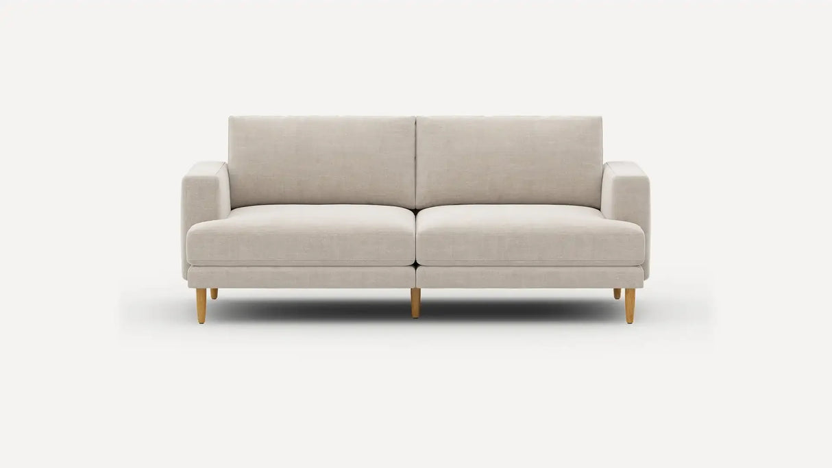 The Ember Mid-Century Modern 75" Sofa, featuring a sleek beige design and wooden legs, is showcased against a plain white background. It boasts a minimalist style with cushioned seats and armrests.