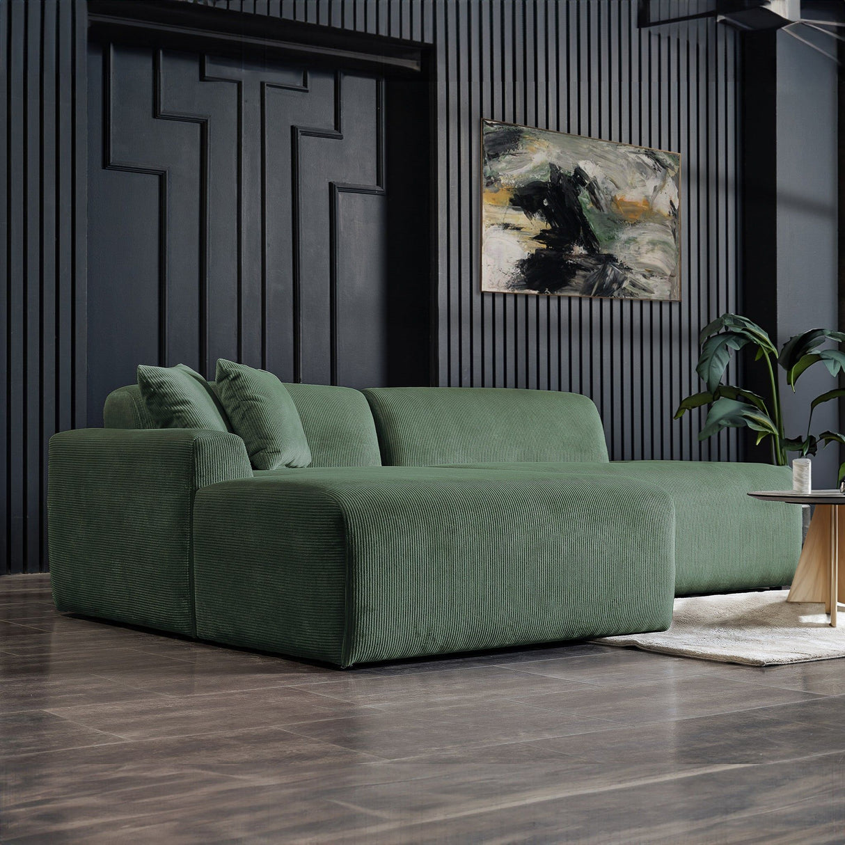 A modern living room showcases the Mar High-Quality Sectional Sofa on a wooden floor. A dark textured wall displays a vibrant abstract painting. A small round table and a plant enhance the decor, creating a cozy, contemporary atmosphere.