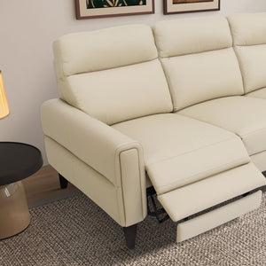 The Elliot Incliner Sofa in beige, with an extended footrest, rests on a textured rug. A black round side table and a warm-toned lamp accompany it, while partial wall art is visible above.