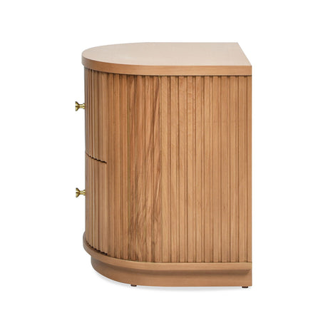 The Valentine - 2 Drawer Storage Side Table features a natural wood finish with a side view displaying a curved design, vertical front slats, and two drawers with brass knob handles, all on a slightly raised base.