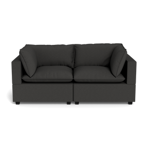 The Kova Pillow Cushion Sofa 86" is a modern dark gray fabric sofa with wide armrests, two large seat cushions, and two matching back cushions, shown from the front against a black background.