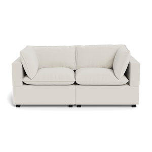 The Kova Pillow Cushion Sofa 86" is a modern, light beige two-seater with wide armrests, plush seat cushions, and two matching back cushions, shown from the front against a plain background.