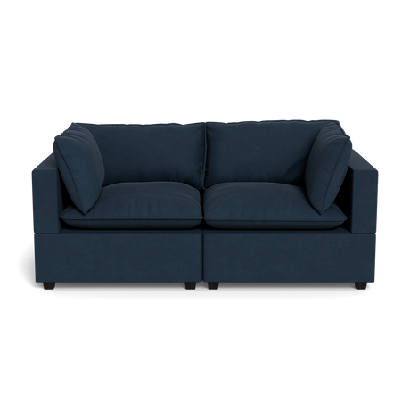 The Kova Pillow Cushion Sofa 86" is a modern, dark blue upholstered sofa with wide armrests and four large cushions, displayed front-facing against a plain black background.