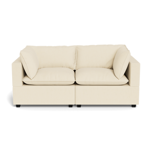 The Kova Pillow Cushion Sofa 86" is a modern, light beige sofa with two seat and back cushions and wide square arms, shown from the front against a plain black background.