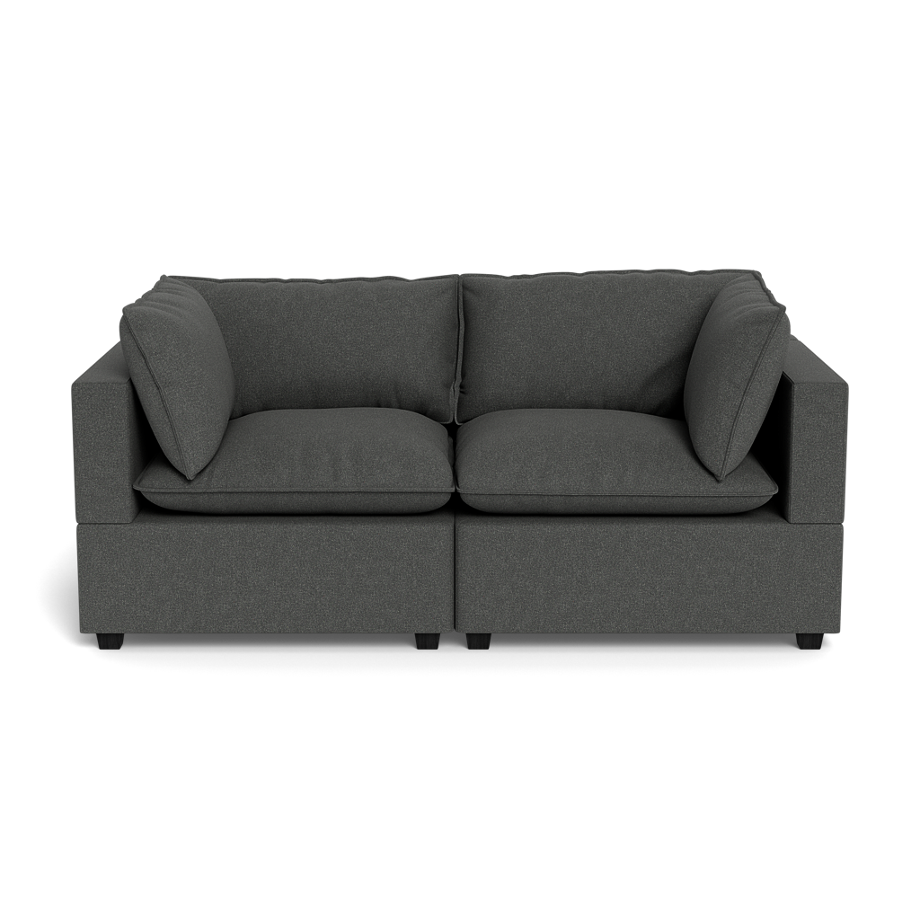 The Kova Pillow Cushion Sofa 86" is a modern dark gray two-seater with wide armrests and four large back cushions, displayed against a black background.