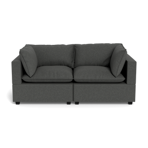 The Kova Pillow Cushion Sofa 86" is a modern dark gray two-seater with wide armrests and four large back cushions, displayed against a black background.