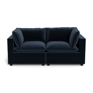 The Kova Pillow Cushion Sofa 86" is a modern dark blue velvet sofa with thick cushions and square armrests, shown from the front against a plain black background.