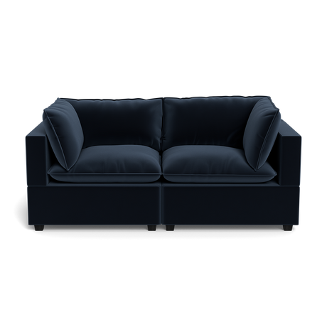 The Kova Pillow Cushion Sofa 86" is a modern dark blue velvet sofa with thick cushions and square armrests, shown from the front against a plain black background.