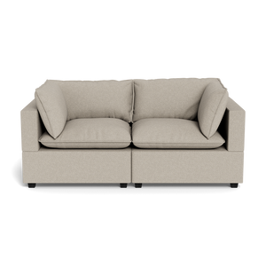 The Kova Pillow Cushion Sofa 86" is a beige, modern two-seater with square arms, plush seat and back cushions, and two matching side pillows, shown from the front against a black background.