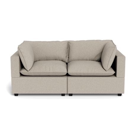 The Kova Pillow Cushion Sofa 86" is a beige, modern two-seater with square arms, plush seat and back cushions, and two matching side pillows, shown from the front against a black background.