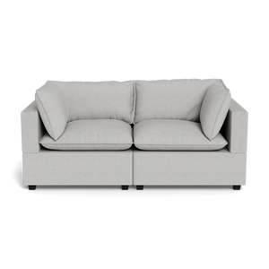 The Kova Pillow Cushion Sofa 86" is a modern light gray two-seater with square armrests, two seat cushions, and two back cushions, displayed against a black background.