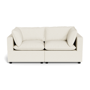The Kova Pillow Cushion Sofa 86" is a modern, cream-colored two-seater with squared arms and two large matching cushions, shown against a black background.